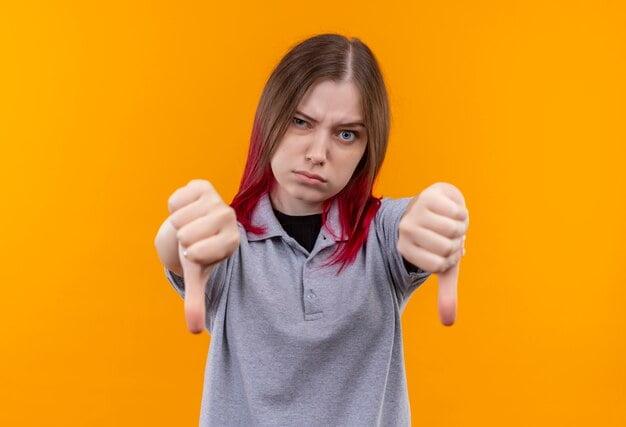 strict young beautiful girl wearing gray t shirt her thumbs down isolated yellow background ()