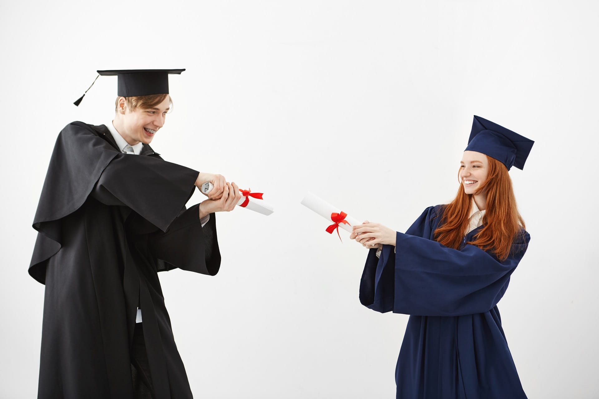 Cheerful graduates smiling fighting with diplomas over white background. Cheerful graduates smiling fighting with diplomas over white background.
